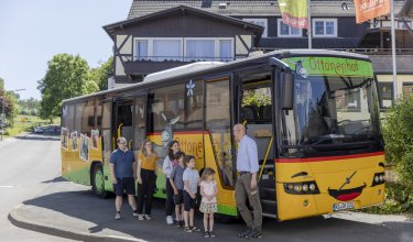 Familie mit Kindern steigt in gelben Bus mit Ottonenhof-Schriftzug vor Fachwerkhaus ein