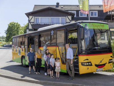 Familie mit Kindern steigt in gelben Bus mit Ottonenhof-Schriftzug vor Fachwerkhaus ein