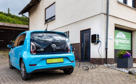 Blaues Elektroauto lädt an Wandladestation neben Haus mit Schild 'Iggemannshof Landappartements'