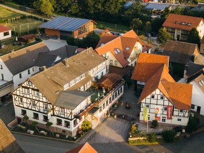 Luftaufnahme eines Dorfes mit Fachwerkhäusern, roten Dächern und grüner Landschaft im Hintergrund