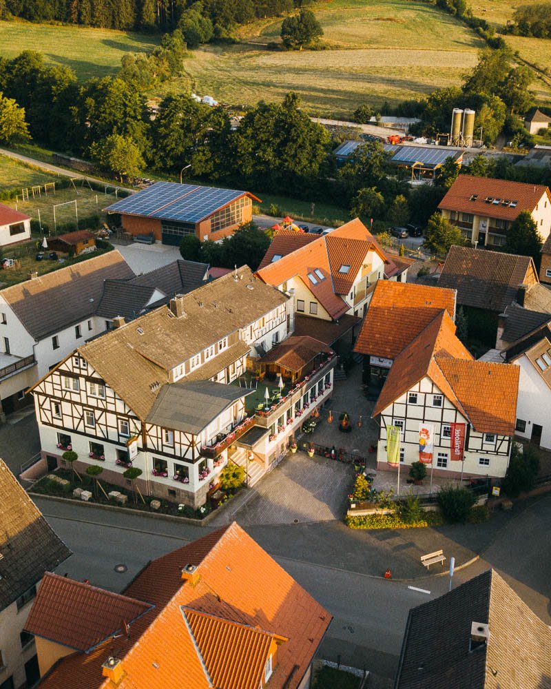 Luftaufnahme eines Dorfes mit Fachwerkhäusern, roten Dächern und grüner Landschaft im Hintergrund