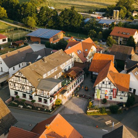 Luftaufnahme eines Dorfes mit Fachwerkhäusern, roten Dächern und grüner Landschaft im Hintergrund