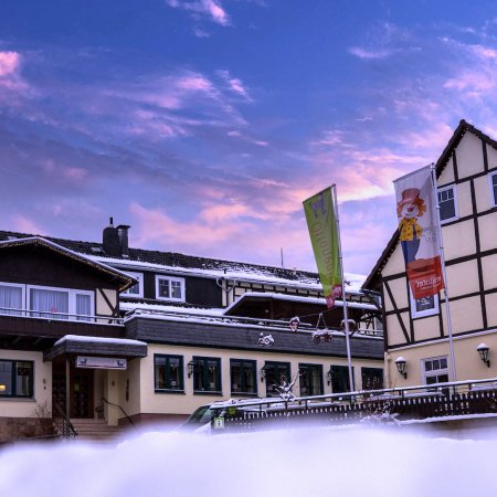 Schneebedecktes Fachwerkhotel bei Sonnenuntergang mit bunten Fahnen und winterlicher Landschaft