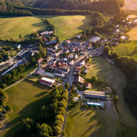 Luftaufnahme eines kleinen Dorfes mit Häusern, Feldern und Wäldern im Abendlicht