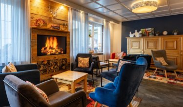 Gemütlicher Wohnraum mit Kamin, mehreren Sesseln und Holzmöbeln, dekoriert mit Kissen und Pflanzen