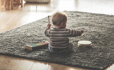 Kind sitzt auf grauem Teppich und spielt mit Xylophon und Tamburin