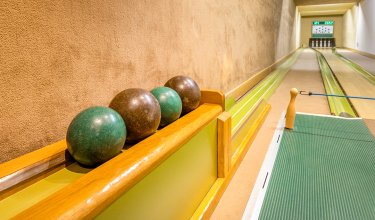 Blick auf eine Kegelbahn mit vier Kegelkugeln auf einem Holzablage und Kegeln am Ende der Bahn