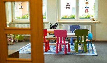 Blick durch eine Tür auf einen Kindertisch mit bunten Stühlen und Spielzeug im Raum