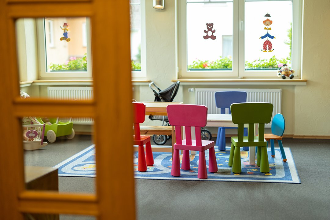 Blick durch eine Tür auf einen Kindertisch mit bunten Stühlen und Spielzeug im Raum