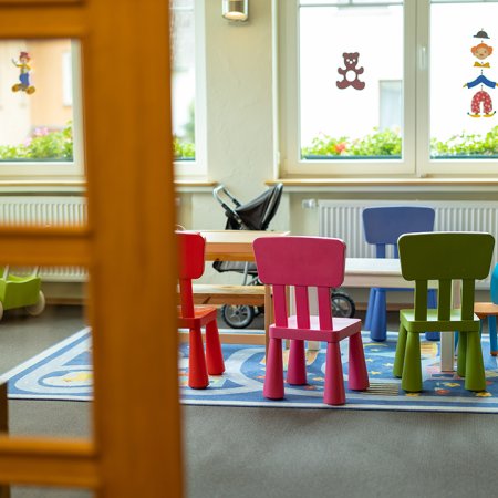 Blick durch eine Tür auf einen Kindertisch mit bunten Stühlen und Spielzeug im Raum