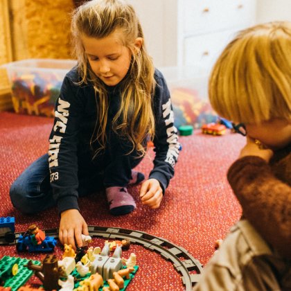 Zwei Kinder sitzen auf rotem Teppich und spielen mit einer Spielzeugeisenbahn und Tierfiguren