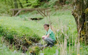 Junge hockt und spielt am Bach