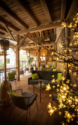 Gemütliche Terrasse mit Holzboden, Sofa, Stühlen mit grünen Kissen und warmen Lichterzweigen