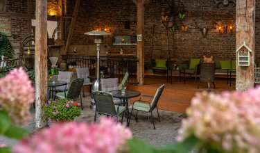 Gemütliche Terrasse mit Tischen, Stühlen und Blumen vor einer Backsteinwand mit Dekoration
