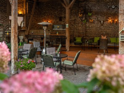 Gemütliche Terrasse mit Tischen, Stühlen und Blumen vor einer Backsteinwand mit Dekoration