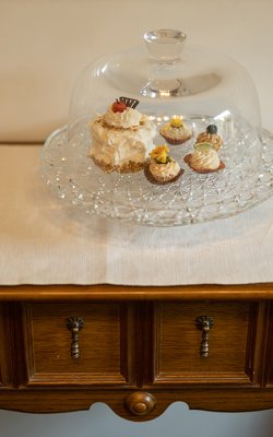 Glasglocke mit kleinen Törtchen auf einem weißen Tuch auf einem Holzschrank