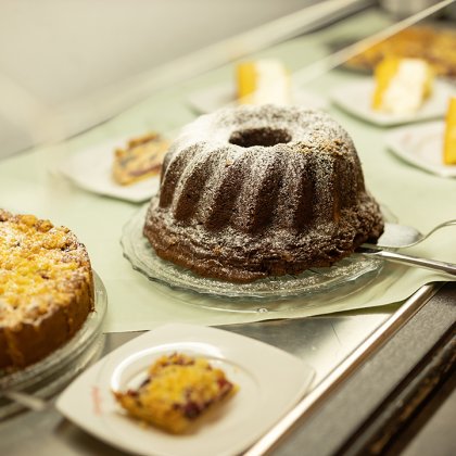 Verschiedene Kuchenstücke und ein Gugelhupf mit Puderzucker auf Glastellern auf einem Tisch