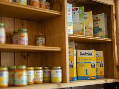 Holzregal mit Babynahrung, darunter Bebivita Anfangsmilch und verschiedene Gläser mit Babybrei