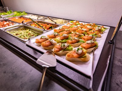 Buffet mit Lachsbrötchen auf einem weißen Teller und verschiedenen Salaten in Metallbehältern