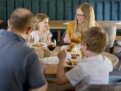 Familie mit zwei Kindern sitzt an einem Tisch und isst gemeinsam in einem Restaurant