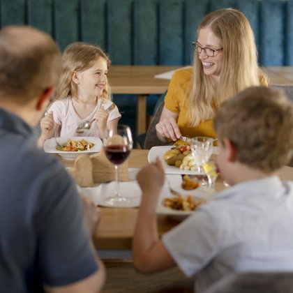 Familie mit zwei Kindern sitzt an einem Tisch und isst gemeinsam in einem Restaurant