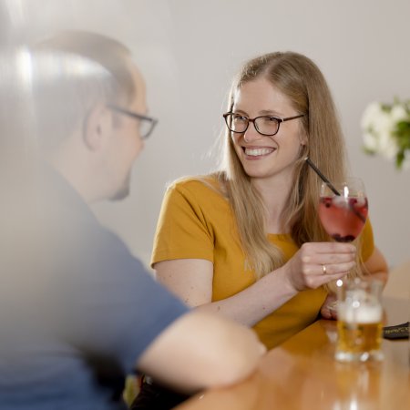 Frau mit Brille und gelbem Shirt hält ein Getränk mit Strohhalm und lächelt einen Mann an