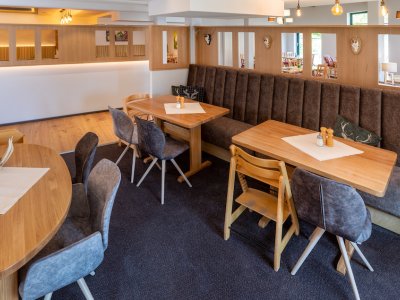 Gemütlicher Gastraum mit Holztischen, gepolsterten Stühlen und brauner Sitzbank an der Wand