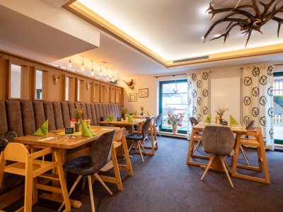 Gemütlicher Gastraum mit Holztischen, grünen Servietten und Hirschgeweih-Deckenleuchte