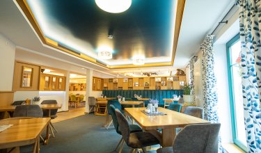 Helles Restaurant mit Holztischen, gepolsterten Stühlen und blauen Vorhängen am Fenster