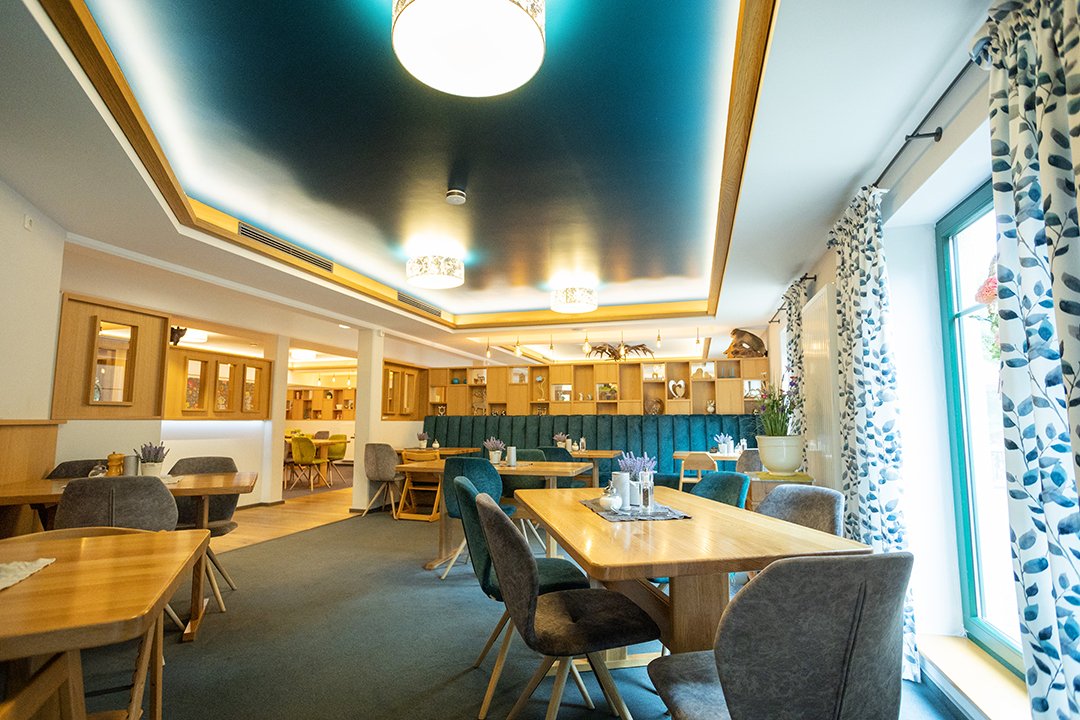 Helles Restaurant mit Holztischen, gepolsterten Stühlen und blauen Vorhängen am Fenster