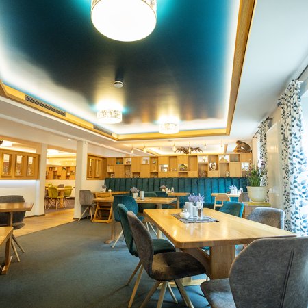 Helles Restaurant mit Holztischen, gepolsterten Stühlen und blauen Vorhängen am Fenster