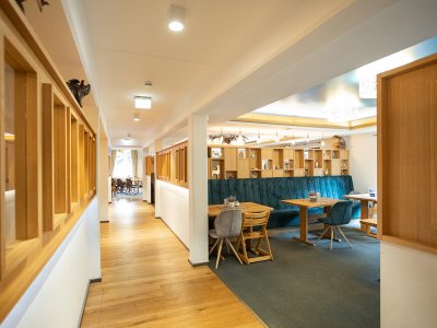 Flur mit Holzboden links und Sitzbereich mit Tischen und blauen Sitzbänken rechts