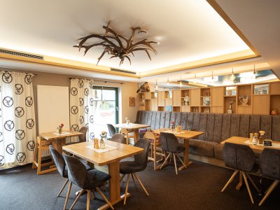 Gemütlicher Gastraum mit Holztischen, gepolsterten Stühlen und Hirschgeweih-Deckenleuchte