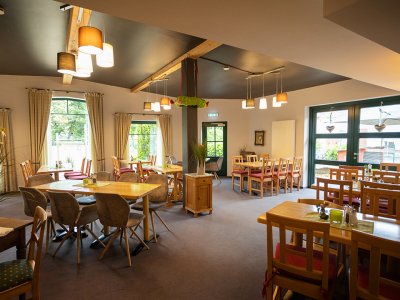 Helles Restaurant mit Holztischen, Stühlen mit roten Polstern und großen Fenstern mit Vorhängen