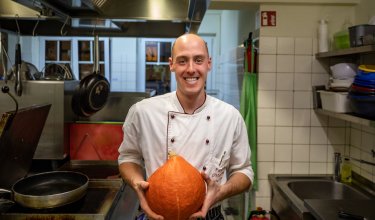 Lächelnder Koch in weißer Jacke hält Kürbis in professioneller Küche