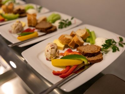 Drei Teller mit Brot, Butter, Paprikastreifen, Frischkäse und Selleriestangen auf einem Glastisch
