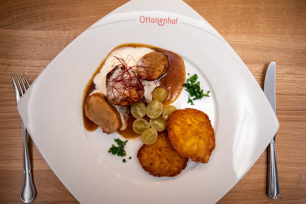 Vorspeise mit Fleisch, Sauce, Trauben, Kräutern und Kartoffelpuffern auf weißem Teller mit Aufschrift Ottonenhof