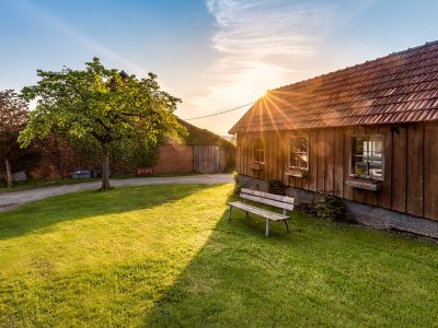 Sonnenuntergang hinter einem Holzhaus mit Bank auf grünem Rasen und Baum links