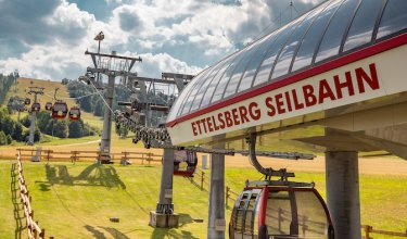 Seilbahnstation Ettelsberg Seilbahn mit Gondeln über grüner Wiese unter bewölktem Himmel