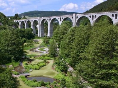 Blick auf ein großes Viadukt mit Bögen über einen grünen Park mit Wegen und Teichen