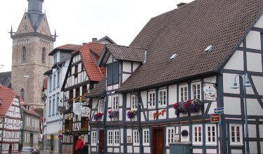 Fachwerkhäuser mit Blumenkästen und ein Kirchturm im Hintergrund in einer Altstadt