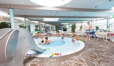 Innenpool mit Planschbecken, Rutsche links, mehrere Kinder und Erwachsene im Wasser und Sitzbereich