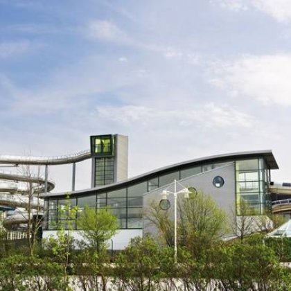 Modernes Schwimmbad mit großer, spiralförmiger Wasserrutsche und Glasfassade unter blauem Himmel