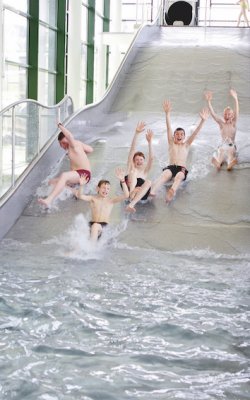 Kinder rutschen fröhlich eine Wasserrutsche in einem hellen Hallenbad hinunter
