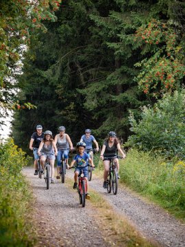 Gruppe von Radfahrern fährt auf einem Waldweg umgeben von grünen Bäumen und Sträuchern