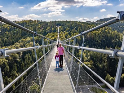 Vogelperspektive auf eine Hängebrücke mit Menschen, die durch einen bewaldeten Talbereich gehen