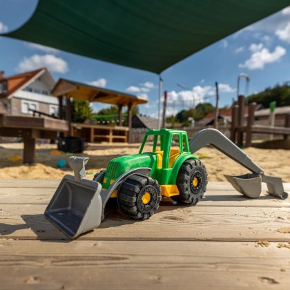 Grüner und gelber Spielzeugbagger auf Holztisch im Sandkasten unter grünem Sonnensegel