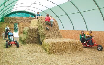 Kinder spielen auf Strohballen im Strohzelt