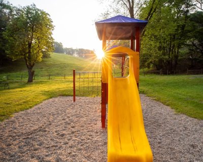 Gelbe Rutsche auf Spielplatz mit Sonnenuntergang und Bäumen im Hintergrund