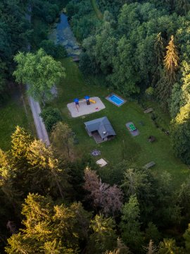 Luftaufnahme eines Spielplatzes mit Rutsche, Sandkasten und kleinem Haus umgeben von Wald